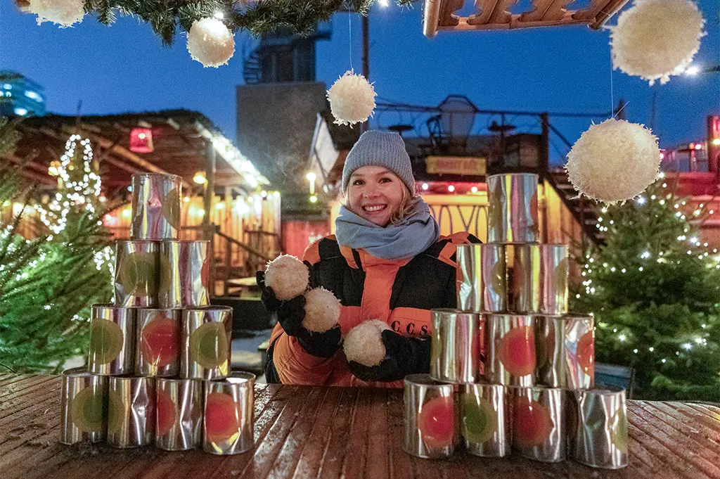 Teilnehmerin am Dosenwurfstand beim mobilen Weihnachtsmarkt-Teamevent in Hamburg – festlich dekoriertes Winterspiel mit Lichterzauber, Spaß und Weihnachtsstimmung