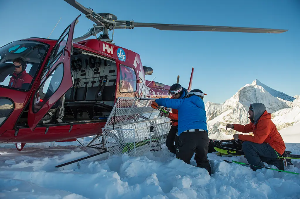 Teilnehmer steigen mit Ski-Equipment aus Helikopter beim Winter-Incentive in der Schweiz – exklusives Heliskiing-Event mit Tiefschnee-Abfahrt, Luxusfeeling und Alpenabenteuer